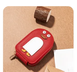 Close-up of a red penguin-shaped leather coin purse with golden zipper on a rustic desk