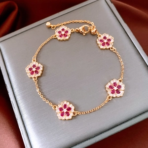 Detailed macro of 18k gold flower bracelet with red zircons on gray jewelry box