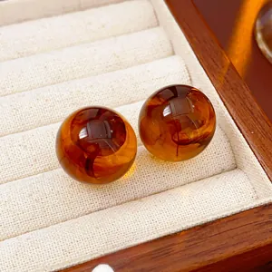 Macro view of round amber resin stud earrings set in a beige velvet jewelry box