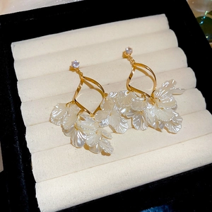 Detail view of gold flower drop earrings with white shell petals and zircon crystals