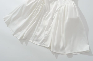 Detalle de vestido de satén blanco con pliegues en la cintura y textura de tela suave