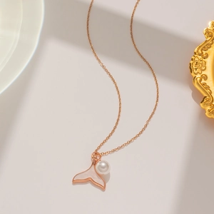 Detailed macro view of gold fish tail pendant with white pearl and mother of pearl inlay