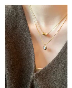 Close-up of layered gold titanium necklace with cylindrical bead and shell pendant