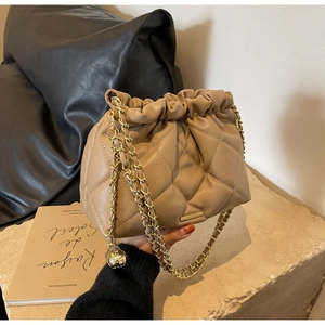 Detail of beige quilted leather bucket bag with gold chain strap on stone display