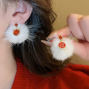 Close-up of white plush ball earrings with a red Fu character pendant and gold trim