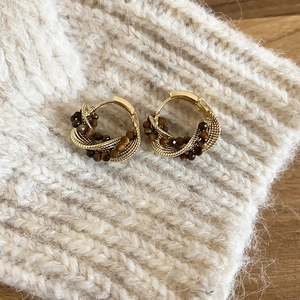Detailed shot of golden twisted triangle earrings with tiger eye beads on knit fabric