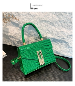 Detail of green crocodile-embossed leather handbag with gold H-shaped clasp and handle