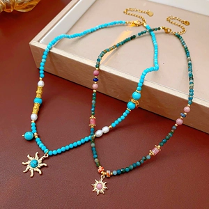 Détail de colliers avec pendentif soleil, pierres turquoise et perles d'eau douce