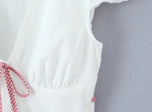 Detail of white embroidered top with floral patterns and red checkered ribbon ties