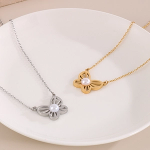 Detail of silver and gold butterfly necklaces with pearl center on a white plate