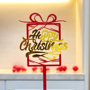 Macro shot of red and gold acrylic Happy Christmas cake topper with festive background