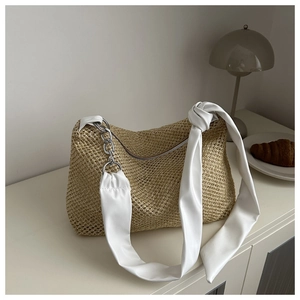 Close-up of woven straw tote bag with white leather straps and metallic chain detail