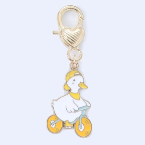 Detail of enamel duck on bicycle charm with golden heart-shaped lobster clasp for bags