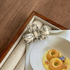 Detail of acetate bow hair claw clip with cream marble texture and gold lettering