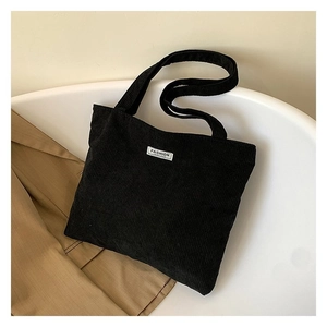 Detail of black corduroy tote bag with white fashion label on a minimalist background