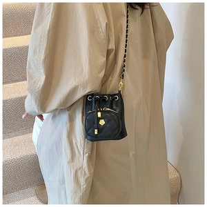Mini black quilted bucket bag with golden camellia floral detail and chain strap worn by model