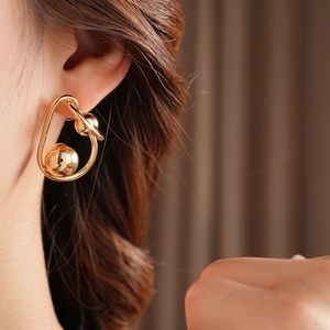 Close-up of gold metal twisted hoop earrings with spherical elements on model ear