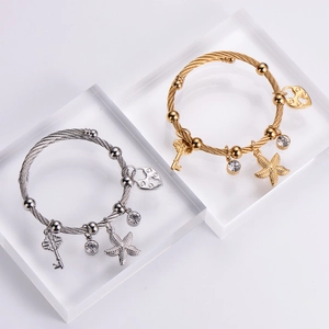 Detail of twisted cable bangles featuring starfish, heart and key charms in gold and silver