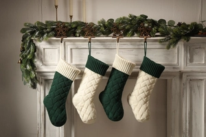 Detail of four knit Christmas stockings in green and cream hanging on a white fireplace