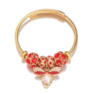 Detail of gold bee charm bracelet with red crystals and white pearl on a reflective surface