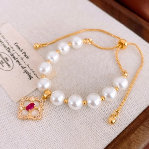 Detailed macro of a vintage gold clover bracelet with pearls and red gemstone on linen