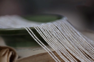 Macro detail of tiny white freshwater pearls draped on a dark green ceramic plate