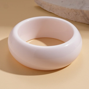 Macro detail of wide cream resin bangle on natural stone and sand background