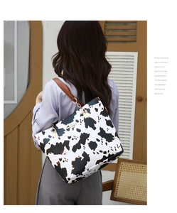 Detail of cow print tote bag with brown leather handles and metallic brand logo plate