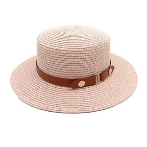 Detail of pink woven boater straw hat with brown faux leather band and gold buckles