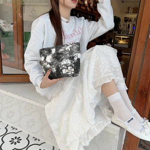Tie-dye canvas pouch with branded label shown in a lifestyle cafe setting with model
