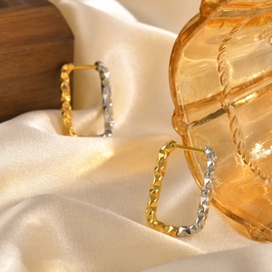 Macro detail of geometric hoop earrings with textured finish on champagne silk background