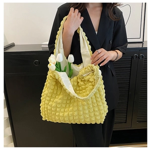 Detail of yellow bubble textured tote bag held by a model in a black suit