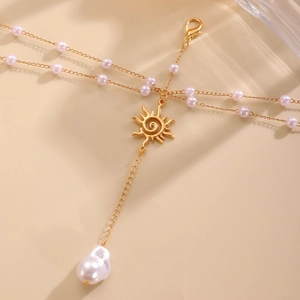Detailed close-up of golden body chain with sun pendant and baroque pearl charms