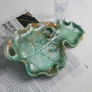 Detail of leaf-shaped green resin tray with golden foils and shimmering glitter texture