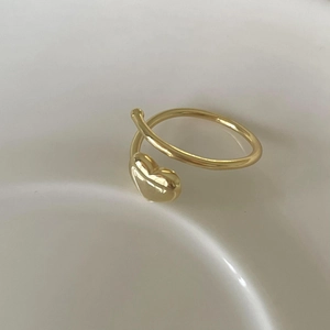 Detailed close-up of a minimalist golden heart-shaped open ring on a ceramic surface