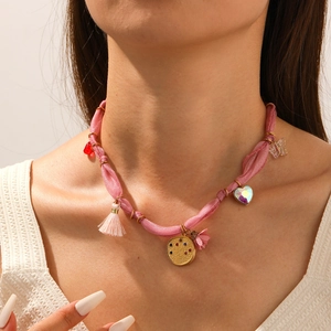Detail of pink fabric necklace with golden pendants and colorful charms worn by a model