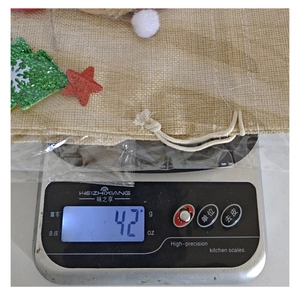 Detailed view of a Christmas burlap drawstring wine bag weighing 42 grams on a digital scale.