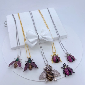Copper insect pendants with colorful cubic zirconia displayed on a white stand