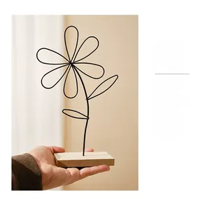 Close-up of a minimalist iron wire daisy ornament on a wooden base held by hand