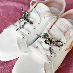 Detailansicht eines grauen Perlenbogens an einem weißen Sneaker mit rosa Akzenten