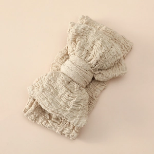 Detail of baby headband featuring large textured beige bow and soft elastic crinkle fabric