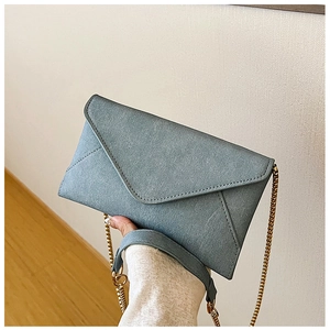 Detail of blue suede envelope bag with fine stitching and golden chain strap