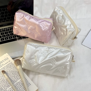 Quilted heart cosmetic bags with bow patterns displayed on a desk with brushes