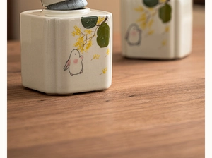 Detailed view of white ceramic tea canister featuring hand-painted rabbit and floral patterns