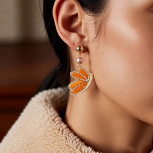 Close-up of model wearing orange butterfly wing earrings with pearls and crystals