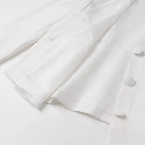 Detail of white blazer hem with fabric-covered button and fine stitching quality