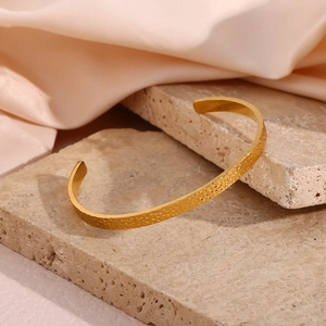 Detailed macro shot of 18K gold-plated hammered texture open cuff bracelet on stone