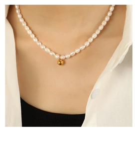 Close-up of baroque pearl necklace with gold sphere pendant on a model's neck
