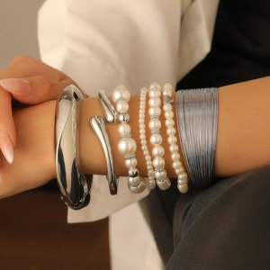 Detail view of stacked pearl bead bracelets and silver metal bangles on a woman's wrist