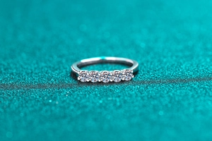 Close-up of five round-cut moissanite stones set in a polished silver wedding ring band